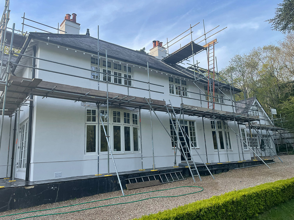 A large white house with scaffolding on the roof and walls, as renovations take place to add external wall insulation.